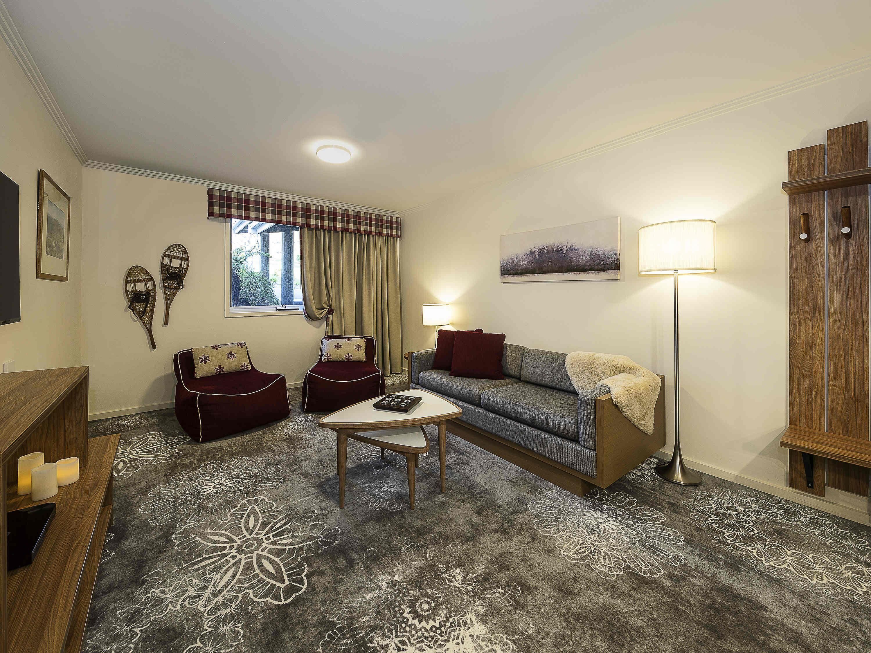 A living room with a sofa, two armchairs, a coffee table, a floor lamp, and a window with curtains.