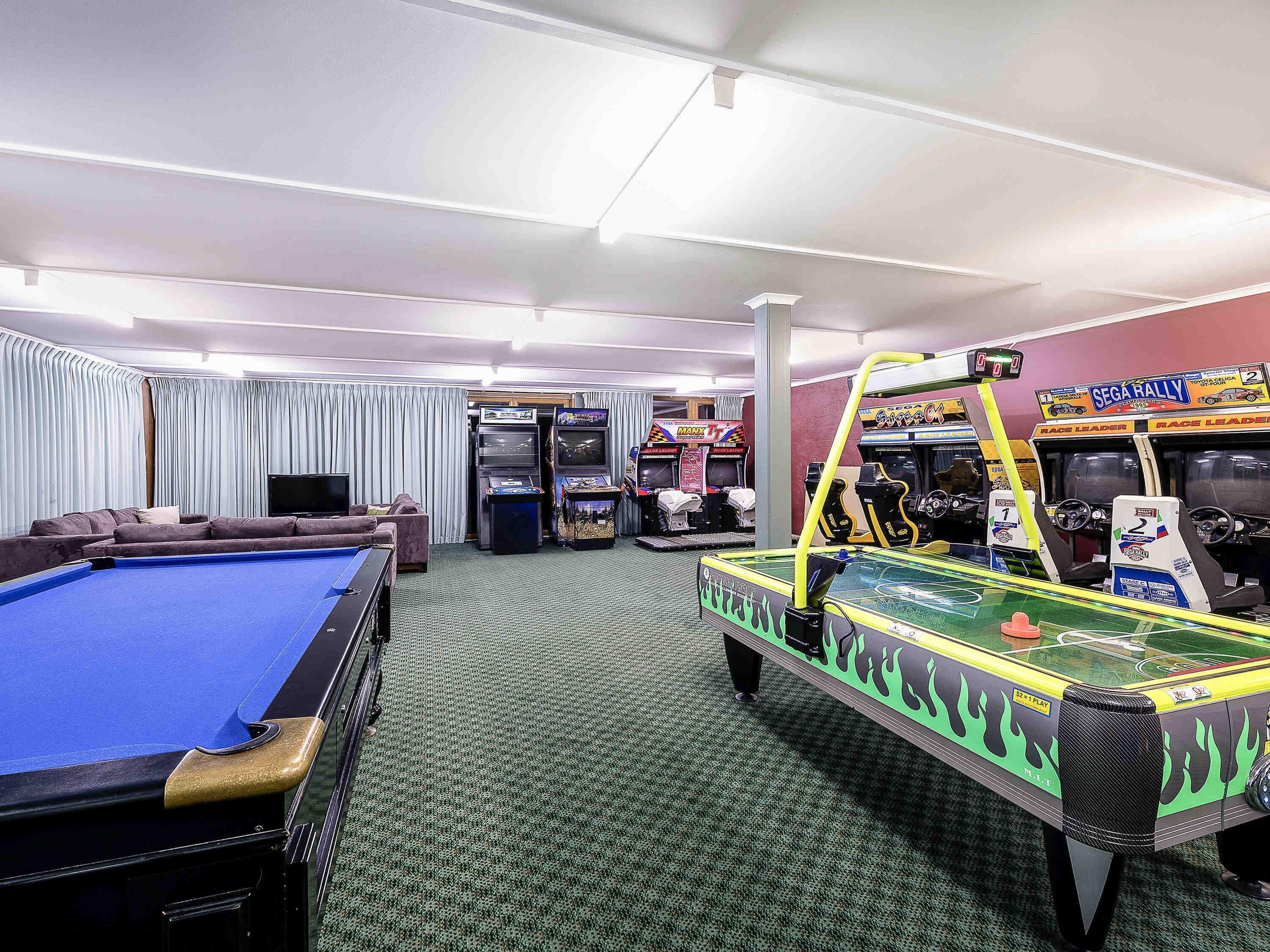 A pool table, arcade games, and a sofa in a room with a carpeted floor.
