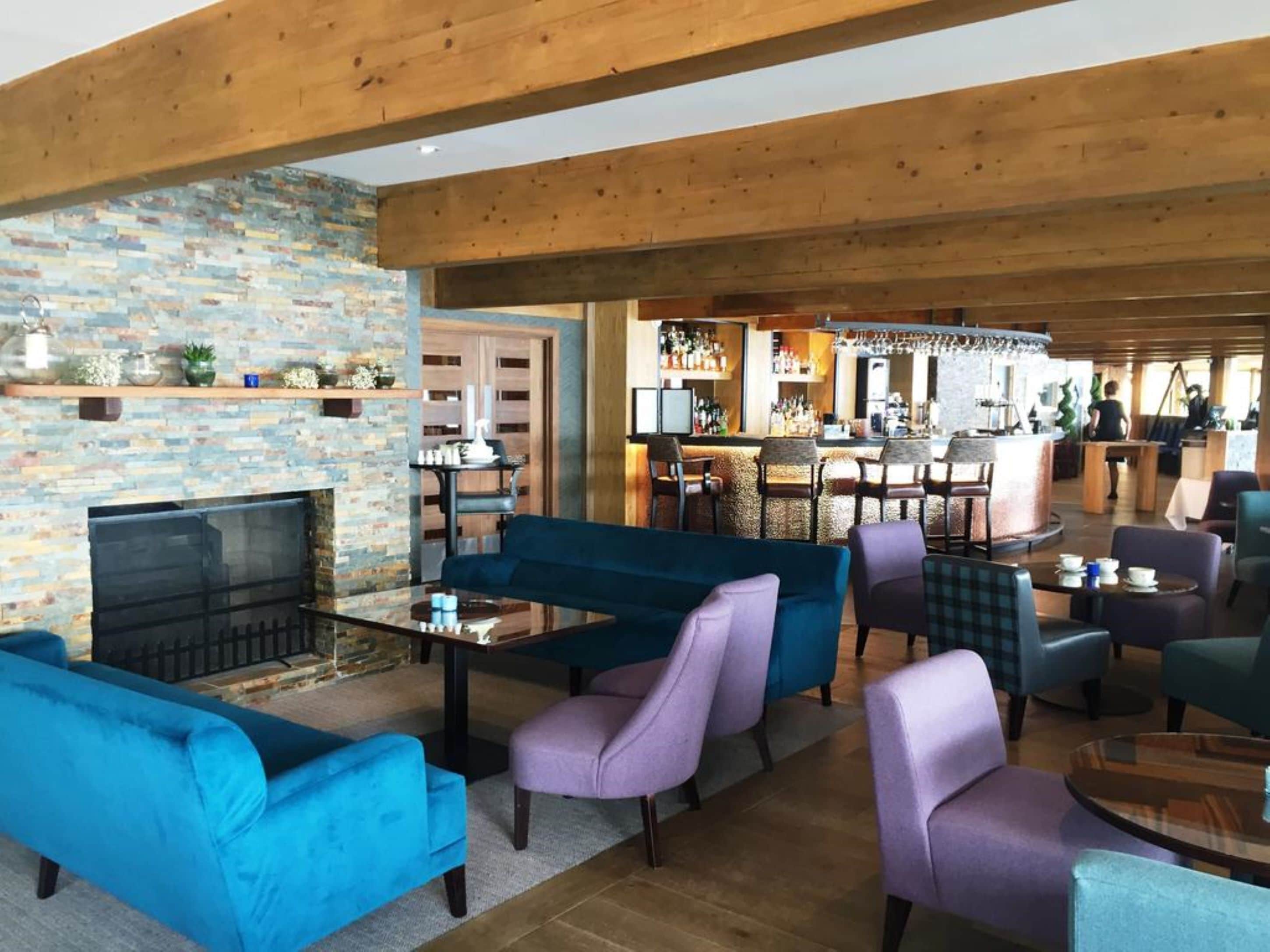 Un salón amplio con chimenea de piedra, sofás azules y morados, una zona de bar con mostrador y un área de estar con una mesa redonda.