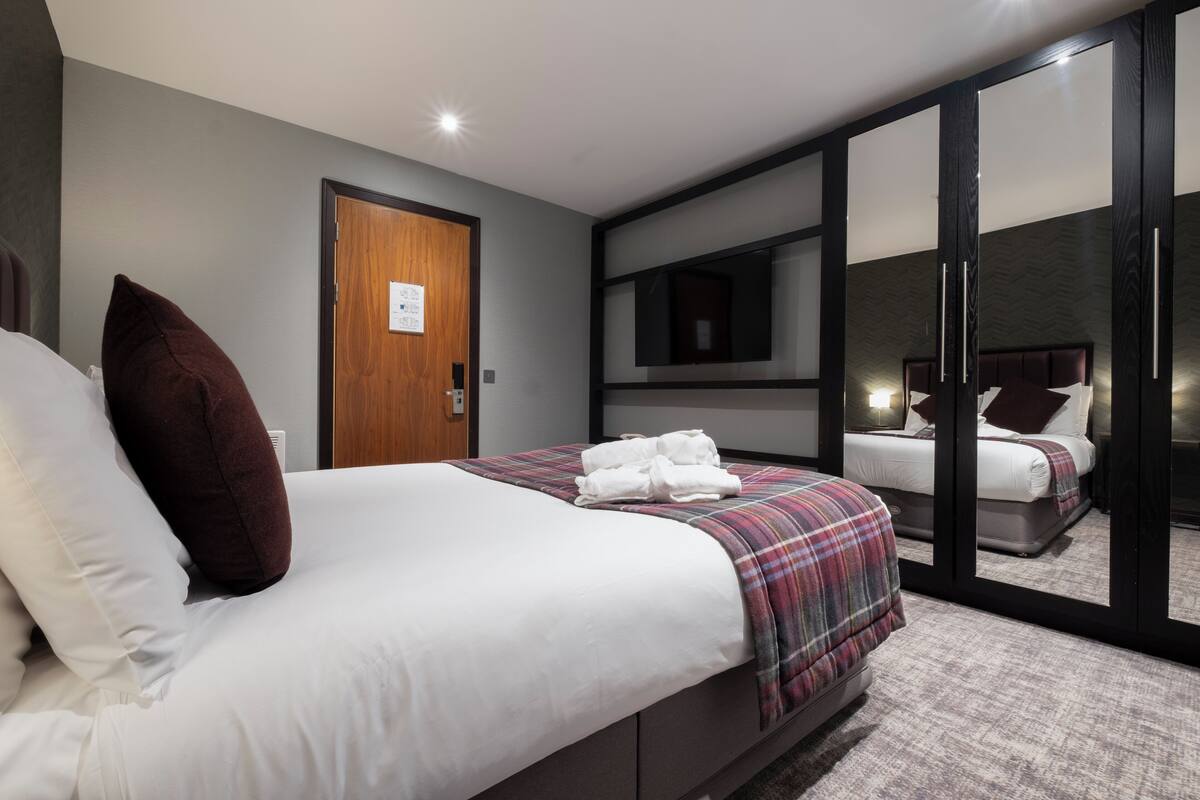 A modern hotel room with a large bed, a wardrobe, a mirror, and a door.