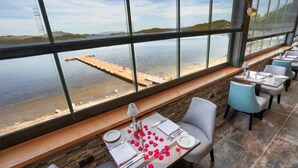 Un restaurante con vistas a un muelle y al agua, con una mesa adornada con pétalos de rosa roja, platos blancos y cubiertos.