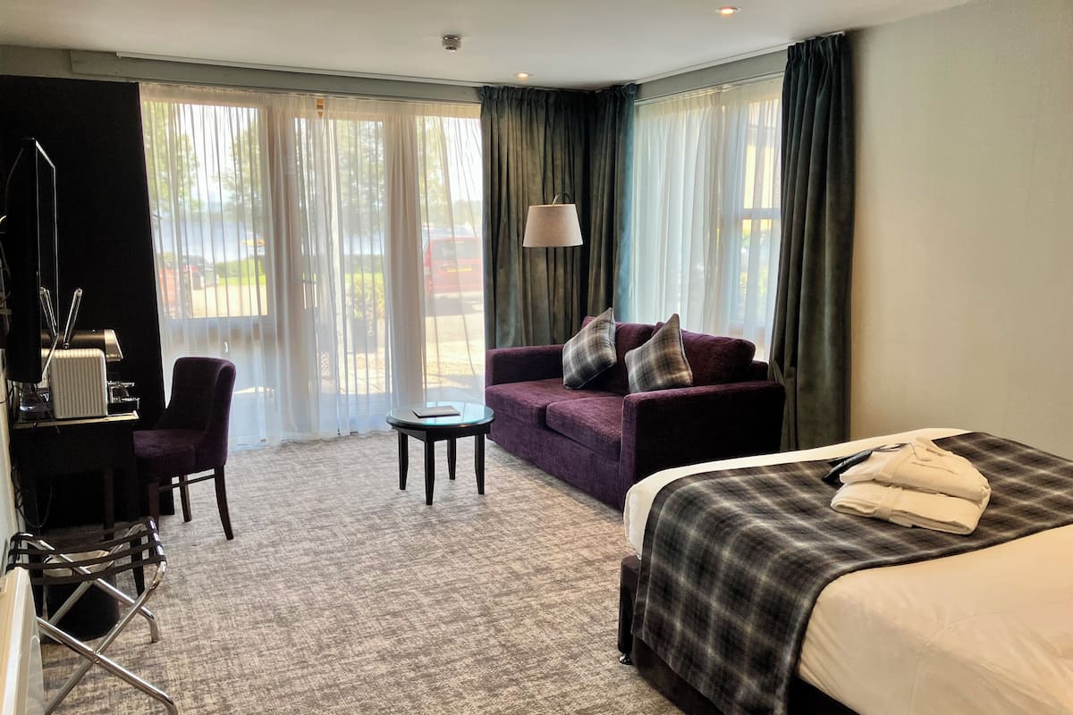 A hotel room with a bed, a sofa, a desk with a computer, and a chair.