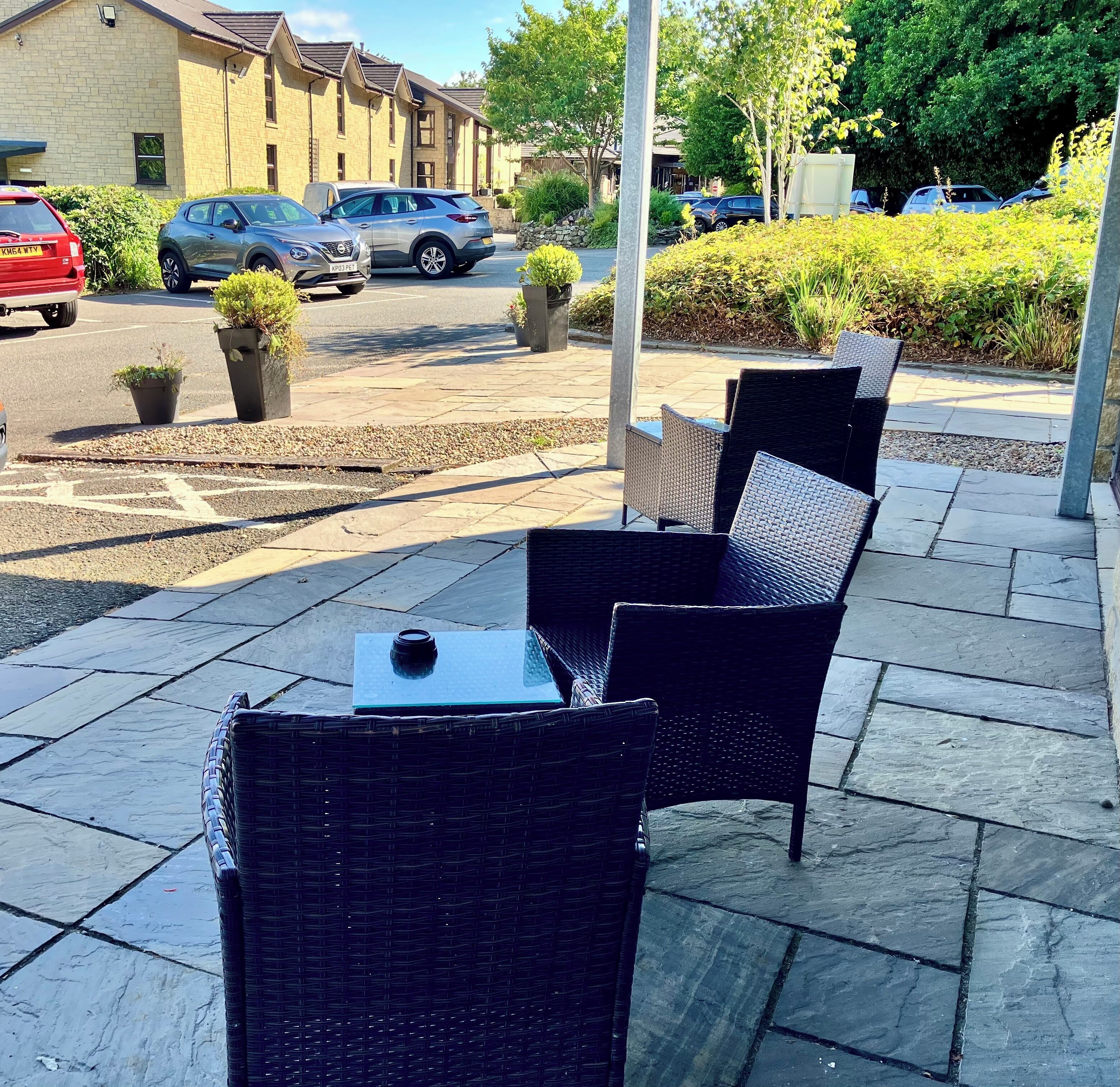 Outdoor wicker furniture on a paved patio with a view of parked cars and buildings in the background.