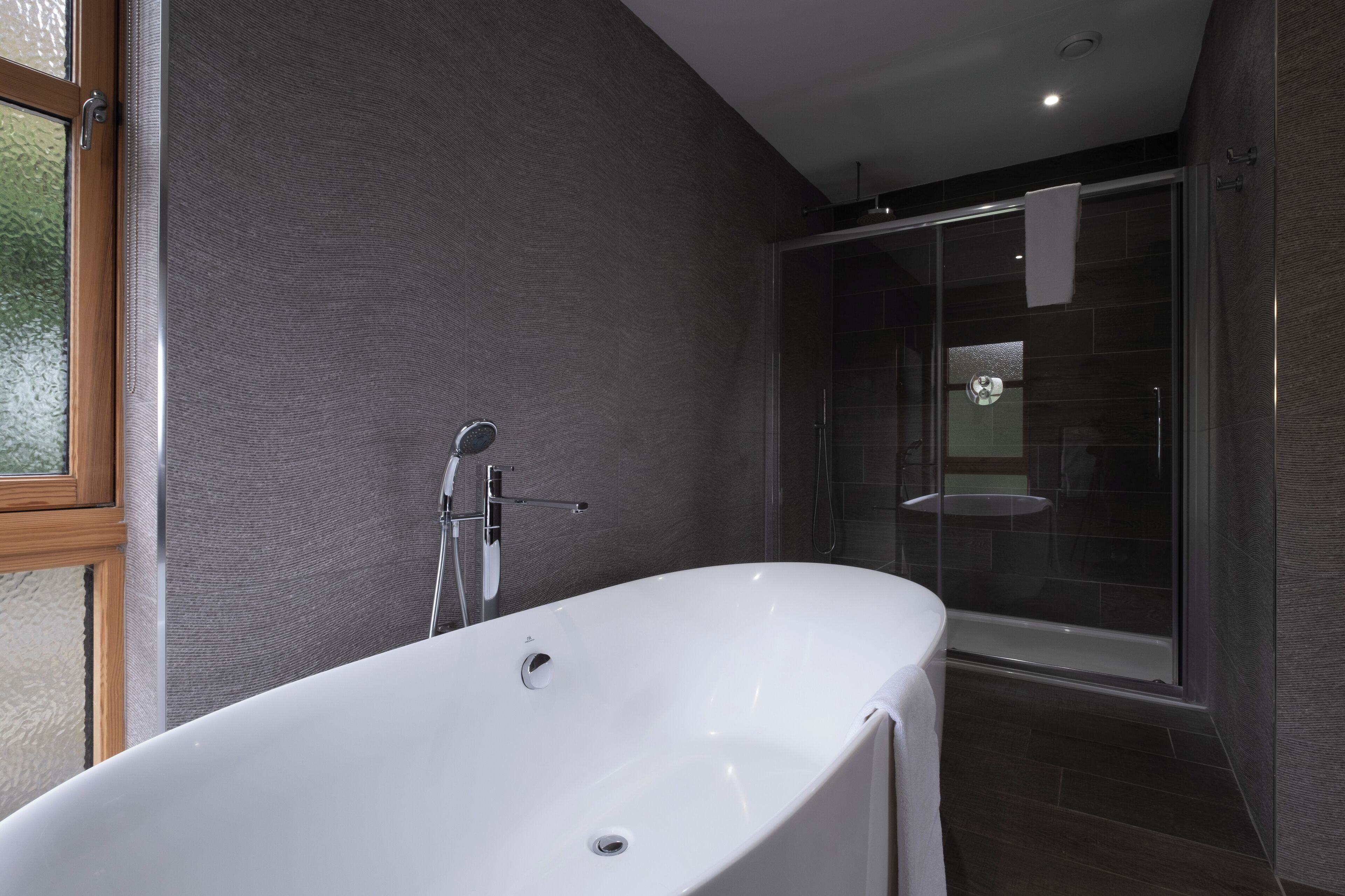 A modern bathroom with a freestanding bathtub, a glass shower enclosure, and a window providing natural light.