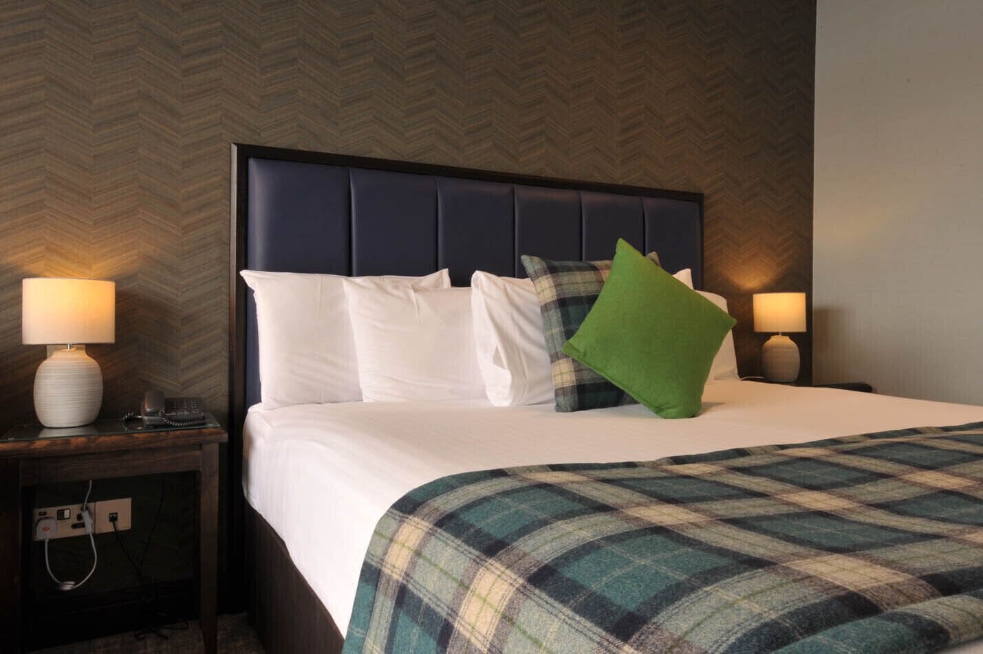 Ein Hotelzimmer mit einem großen Bett, einem Kopfteil, zwei Nachttischen und zwei Lampen.