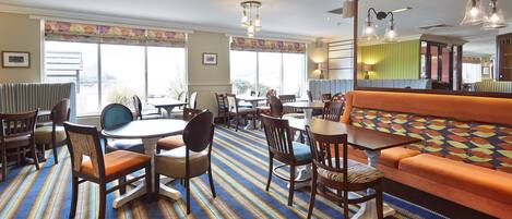 A dining area with striped carpet, wooden tables, chairs, and an orange sofa.