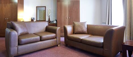 A hotel room with two leather sofas, a wooden wardrobe, a small table, and a mirror.