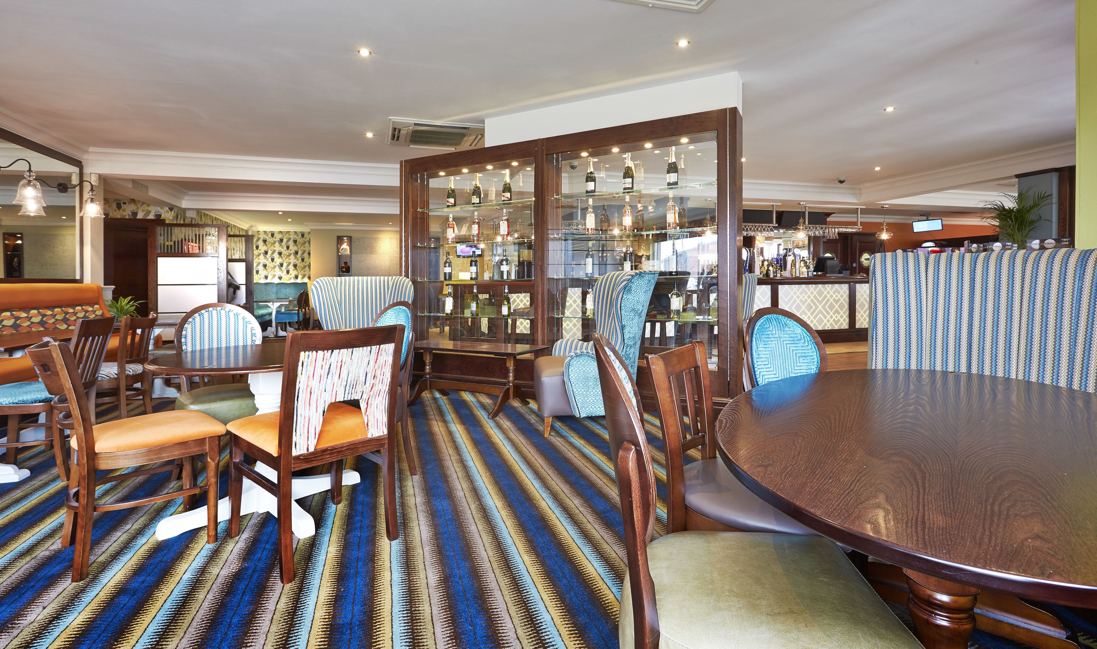 A restaurant with a bar area, wooden furniture, and a patterned carpet.