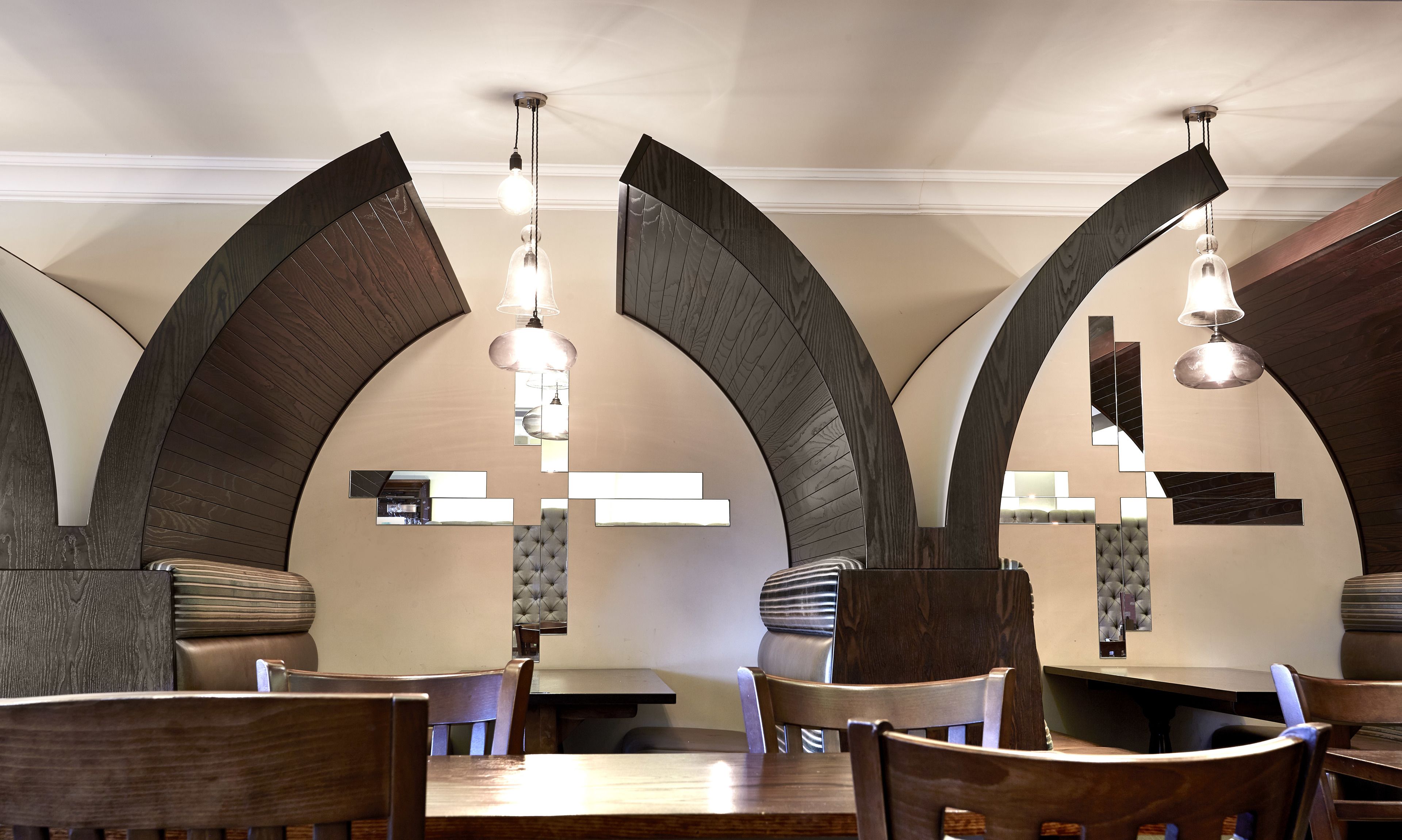 A restaurant interior with high arched ceilings, wooden furniture, and pendant lighting.