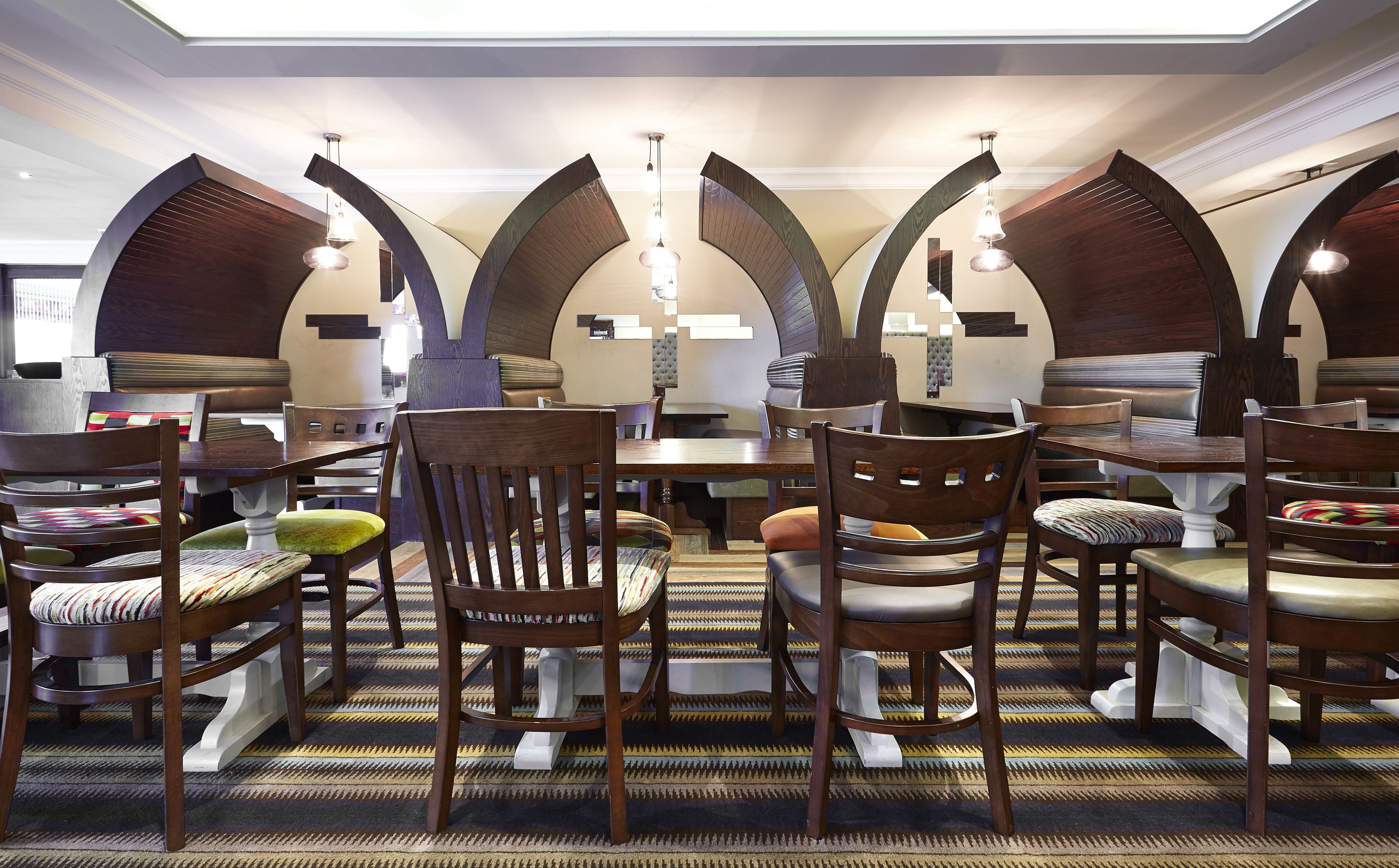 A dining area with multiple tables and chairs, featuring a patterned carpet and wooden furniture.