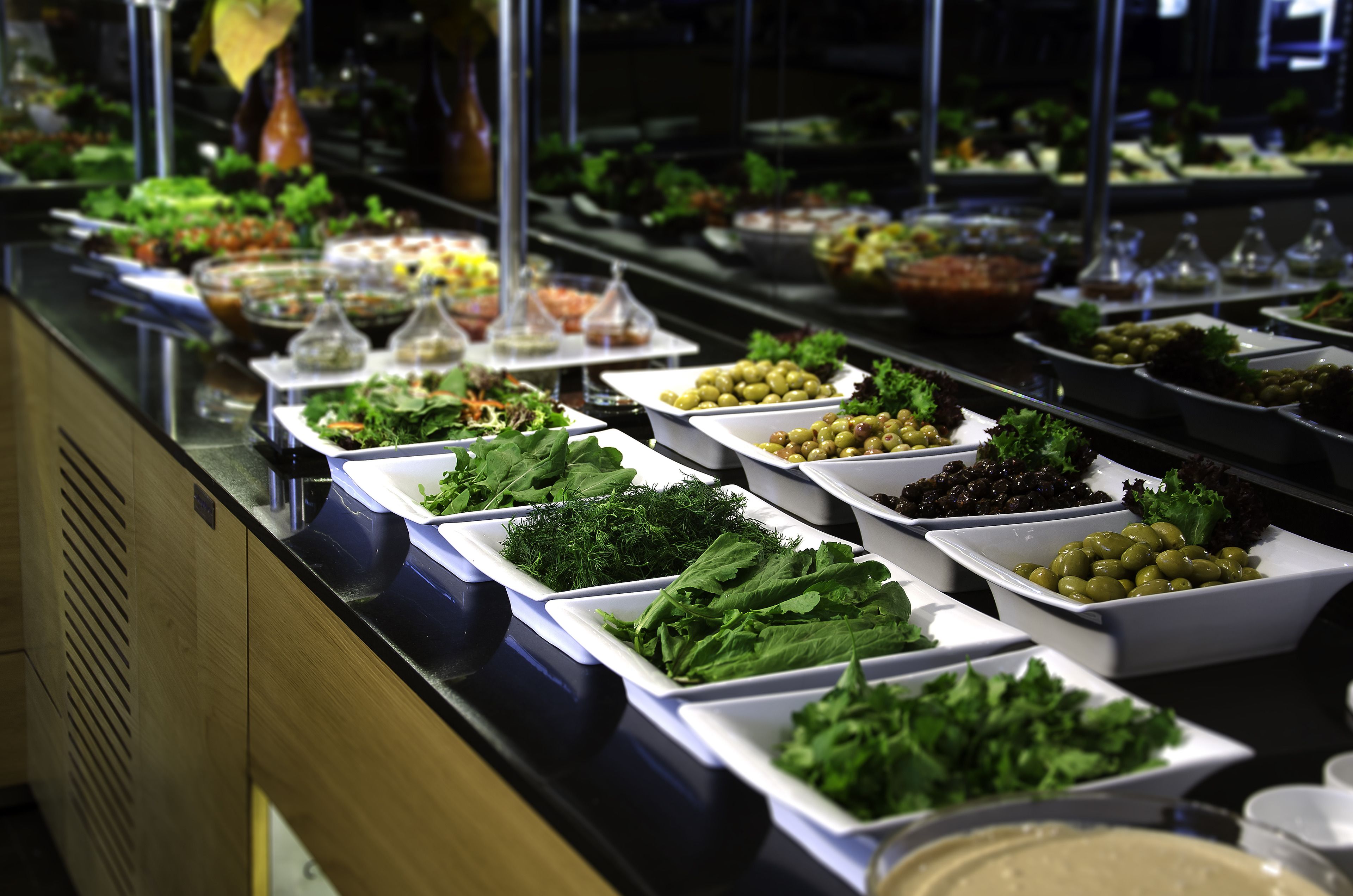 Un buffet proposant une variété de plats, notamment des salades, des légumes verts et des olives.