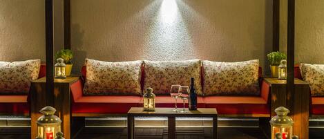 A cozy seating area with a sofa and cushions, a small table with a bottle and glasses, and multiple lanterns providing ambient lighting.