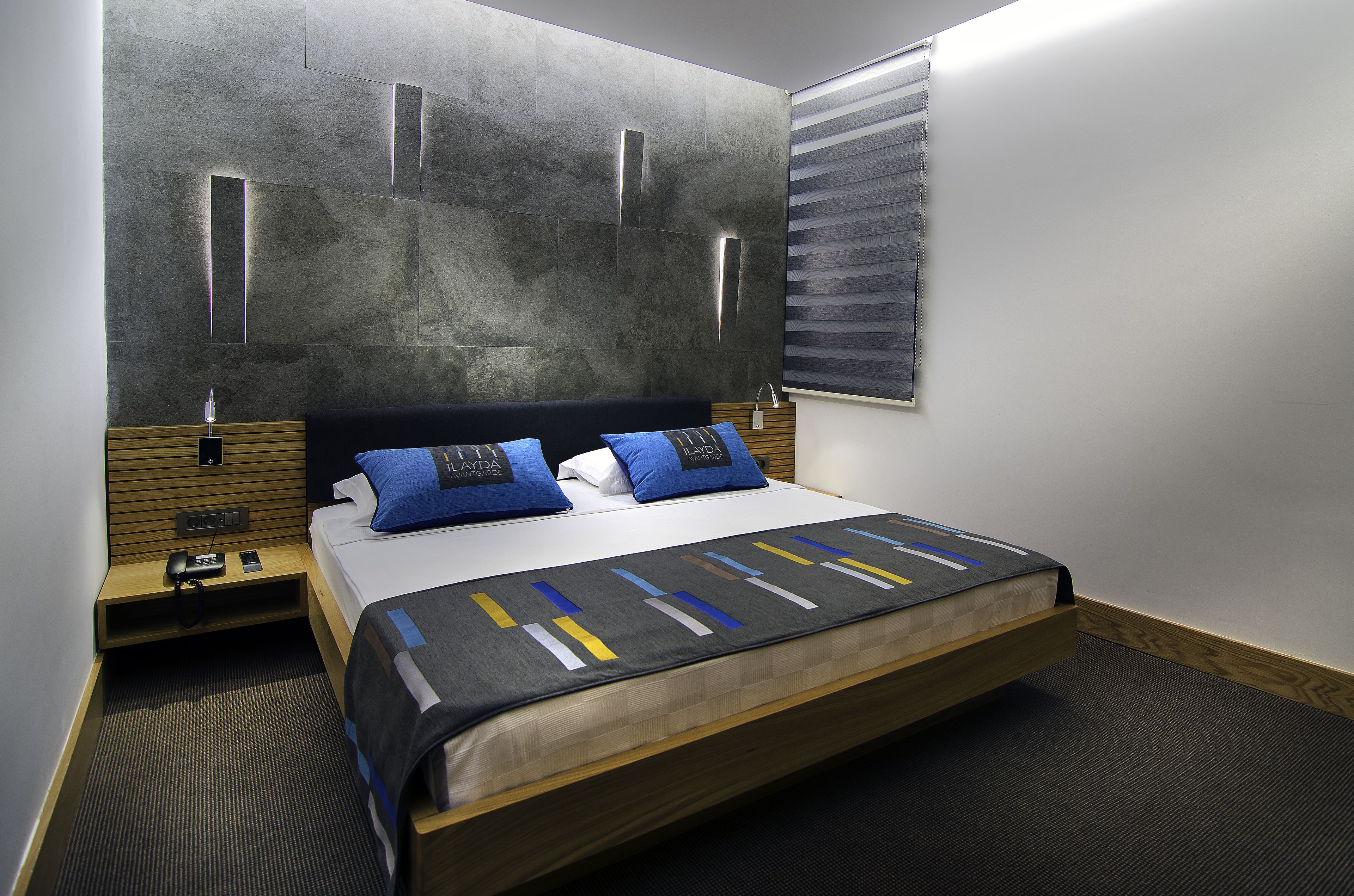 A modern hotel room with a large bed, a wooden nightstand, a bedside table, and a wall-mounted light fixture.