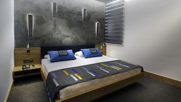 A modern hotel room with a large bed, a wooden nightstand, a bedside table, and a wall-mounted light fixture.