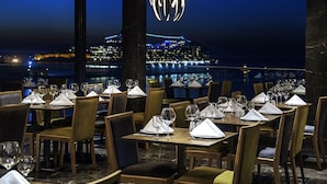 A restaurant with tables set for dining, featuring a view of a cityscape at night. - Ilayda Avantgarde Hotel (Kusadasi)