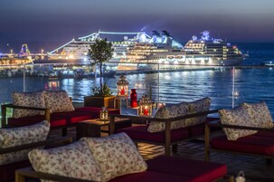Una terrazza con sedute rosse imbottite e lanterne, con vista su una nave da crociera di notte.