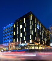 Un hotel moderno con un bar Starbucks al piano terra, caratterizzato da una facciata geometrica originale e finestre illuminate.