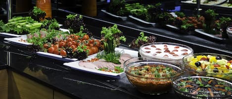 A buffet with various dishes including vegetables, fruits, and salads.