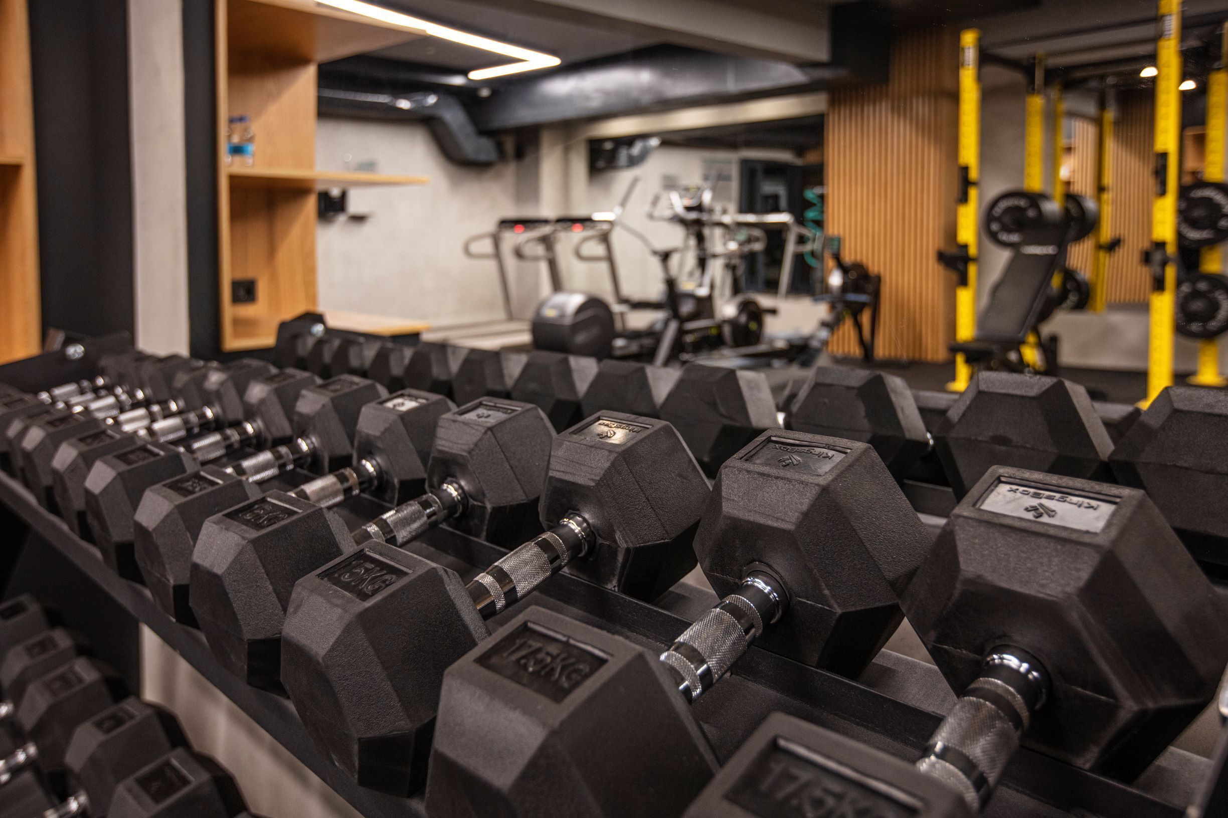 A gym with rows of black dumbbells and weight machines in the background.