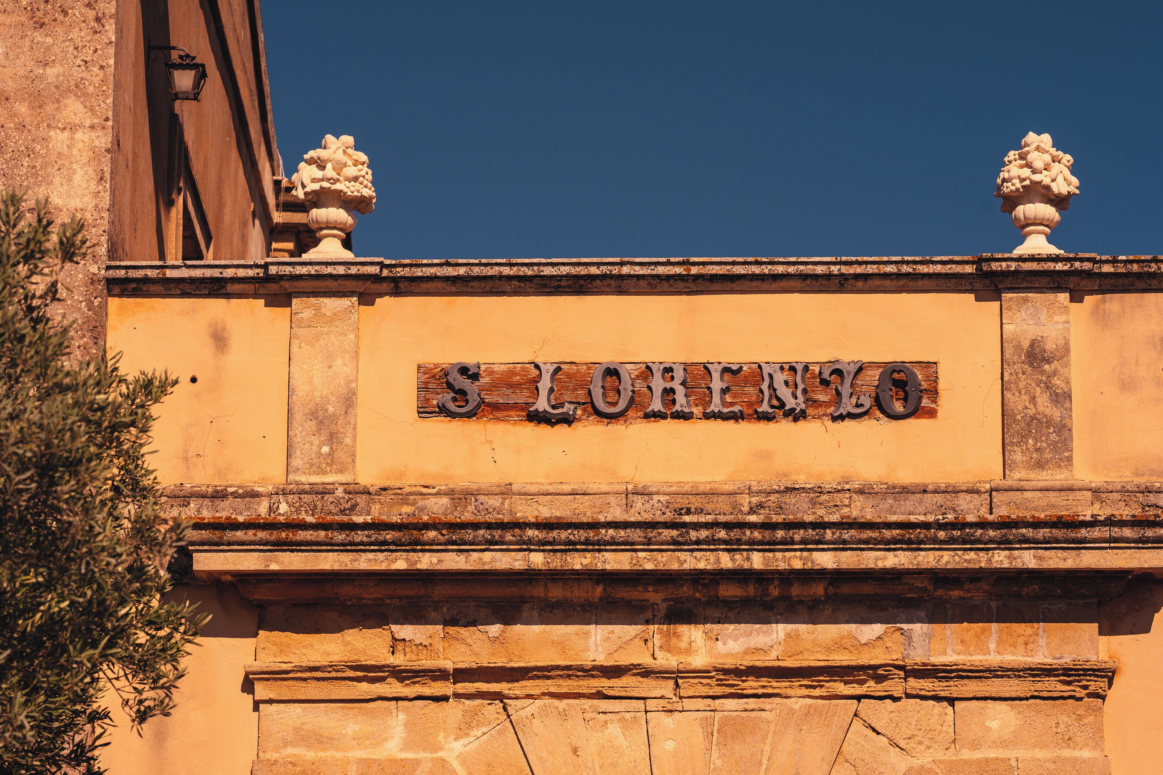 Fachada de edificio con la inscripción “S. Lorenzo” y dos urnas decorativas en la parte superior.