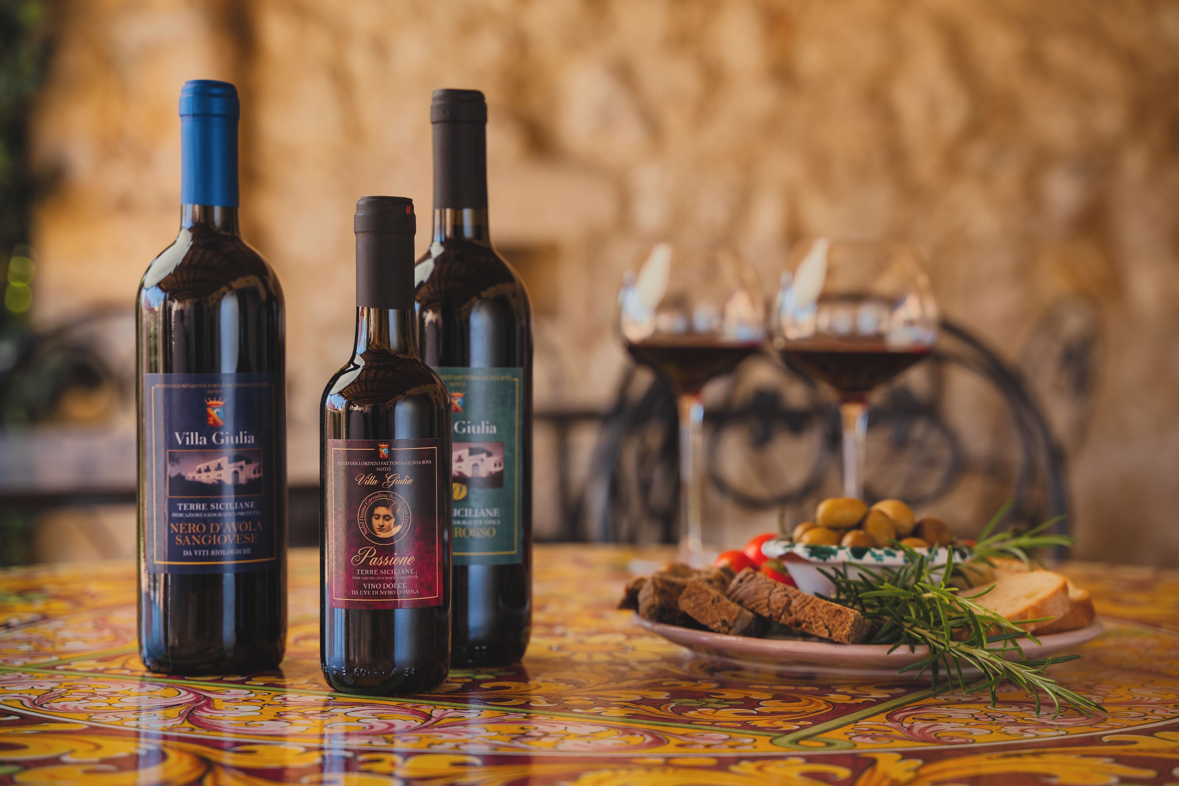 Trois bouteilles de vin sont posées sur une table, accompagnées d’une assiette de nourriture et d’un chandelier en arrière-plan.