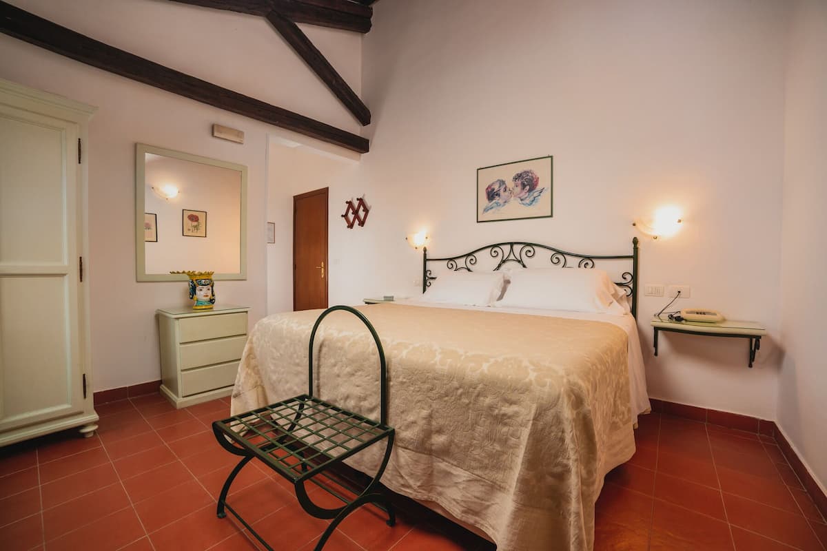 A bedroom with a bed, bedside table, nightstand, and a chair.