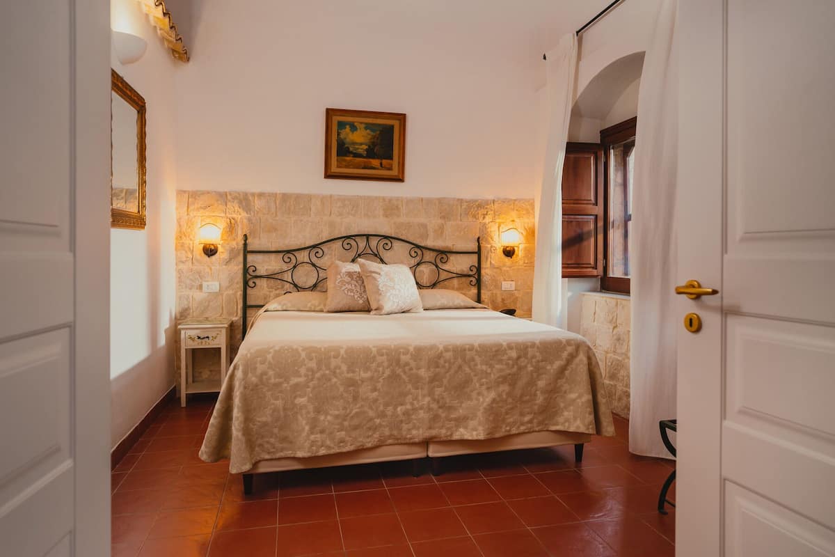 A bedroom with a bed, two nightstands, a wall-mounted light, and a painting.