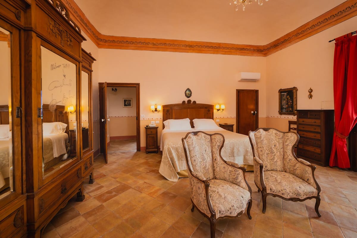 A hotel room with a large bed, two nightstands, a wooden dresser, a mirror, and two upholstered chairs.
