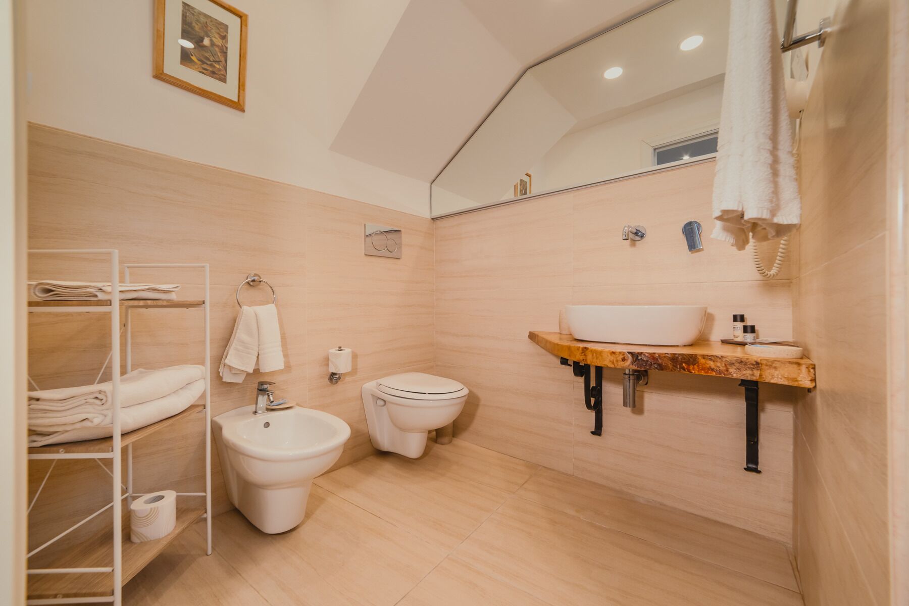 A modern bathroom with a wooden floor, a white sink, a bidet, and a towel rack.