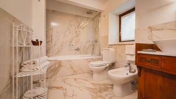 Un baño moderno con piso de mármol, ducha envuelta en vidrio, inodoro, bidé y tocador de madera con lavamanos.
