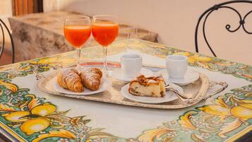 Ein Tisch mit Gebäck, einem Croissant, einer Kuchenstück und zwei Gläsern Orangensaft auf einer bunten Tischdecke.