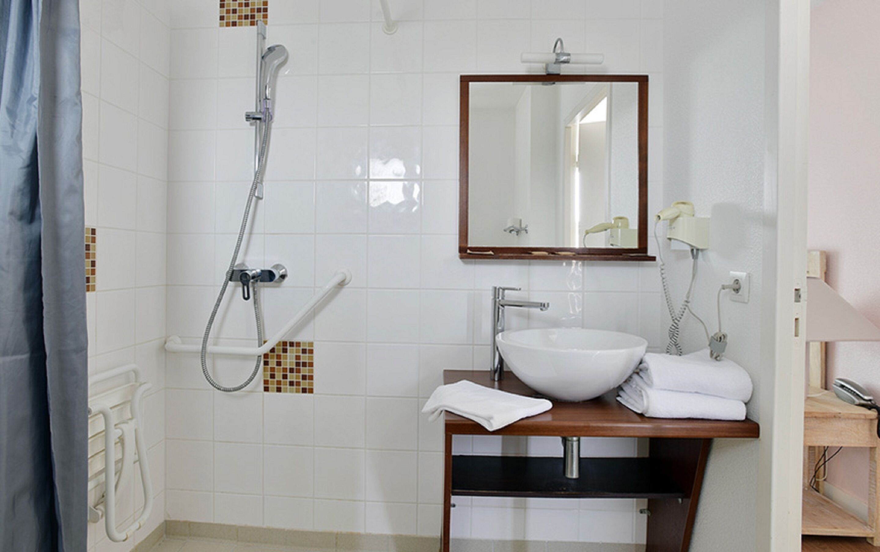 Un baño con lavamanos blanco, un espejo, ducha y perchero.