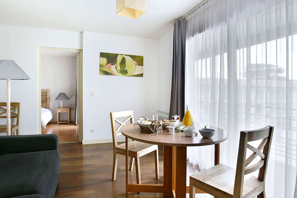 Un salon moderne avec une table de salle à manger ronde en bois, deux chaises, un canapé et une lampe.