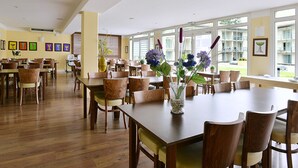 Un vaste espace dédié à la salle à manger, avec des tables et des chaises en bois, de grandes fenêtres et des œuvres d’art encadrées qui ornent les murs.