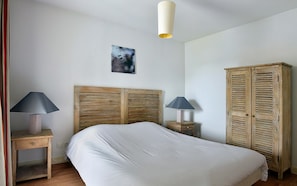 Un dormitorio con una cama grande, dos mesitas de noche con lámparas, un armario de madera y un candelabro en el techo.