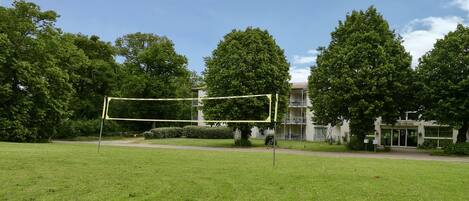 A grassy area with a volleyball net, trees, and a building with a sign reading "Chateau".