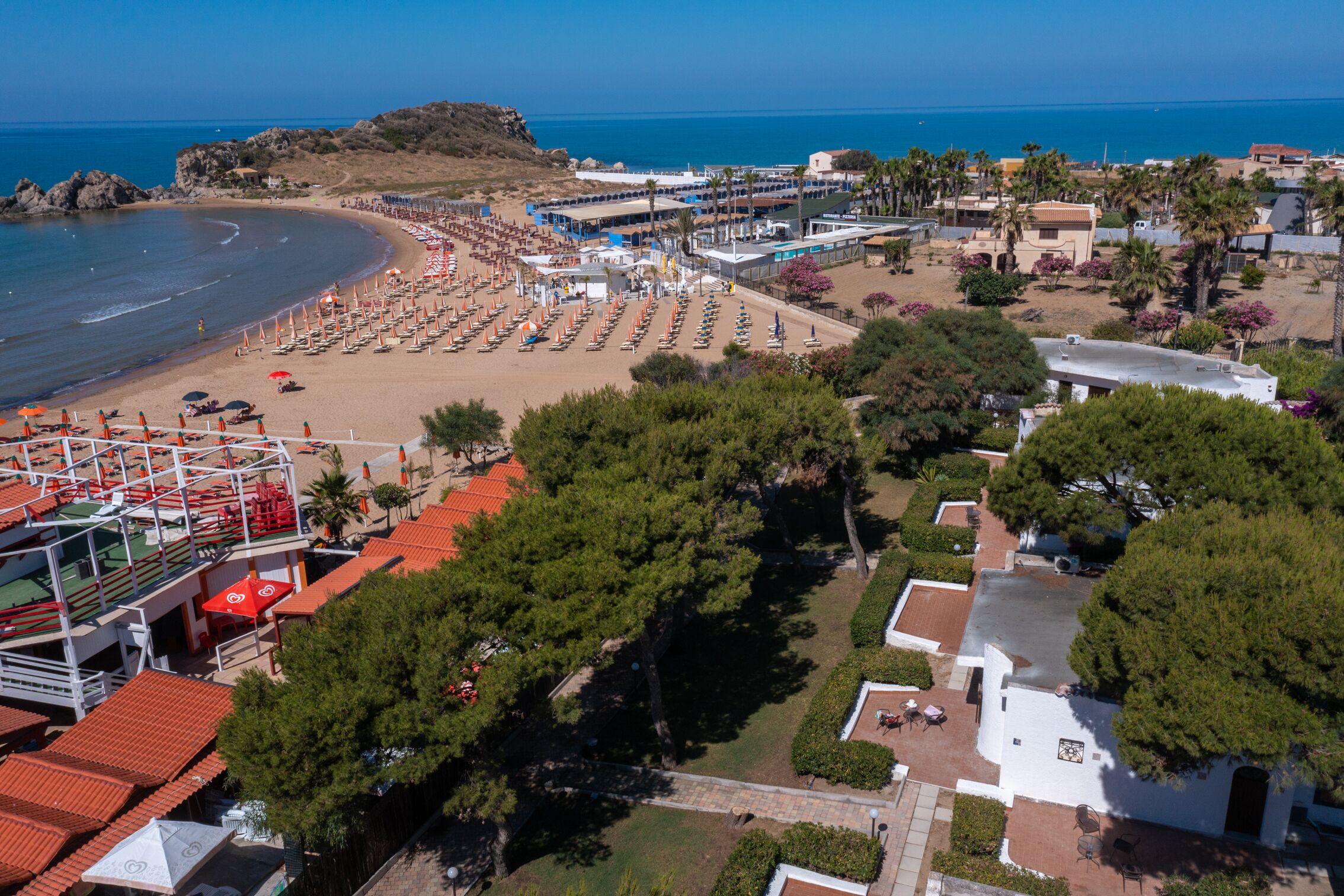 A coastal resort with beach access, multiple villas, and a central building with a swimming pool.