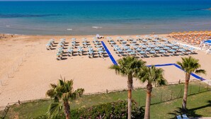 A beach with rows of umbrellas and lounge chairs, a clear blue sky, and the ocean in the background. - Baia D'Oro Hotel (Licata)