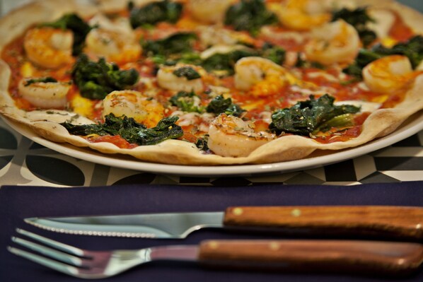 Pizza con camarones y espinacas sobre un plato, con un tenedor y cuchillo a un lado.