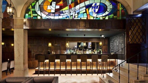 A bar area with a stained glass window, bar stools, and a staircase. - TURIM Restauradores Hotel (Lisbon)