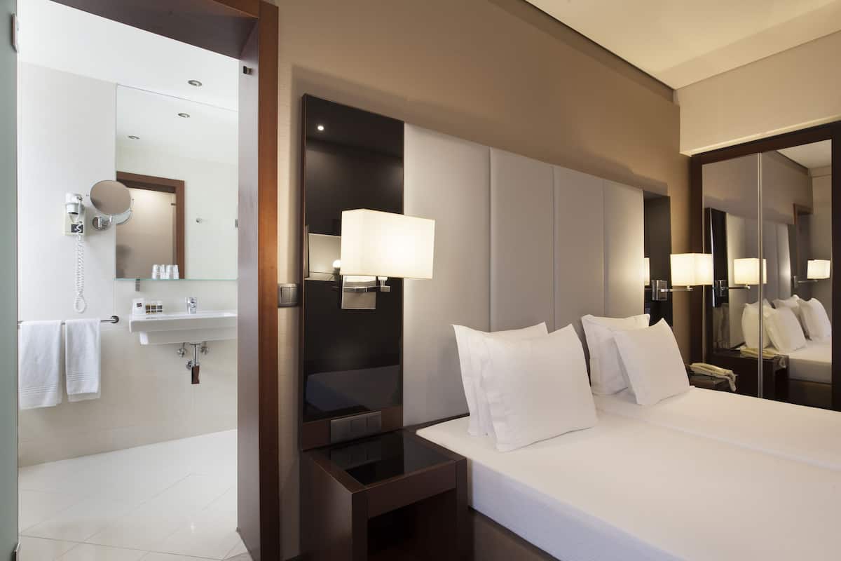 Een hotelkamer met een groot bed, nachtkastje, spiegel, badkamer met wastafel en spiegel.
