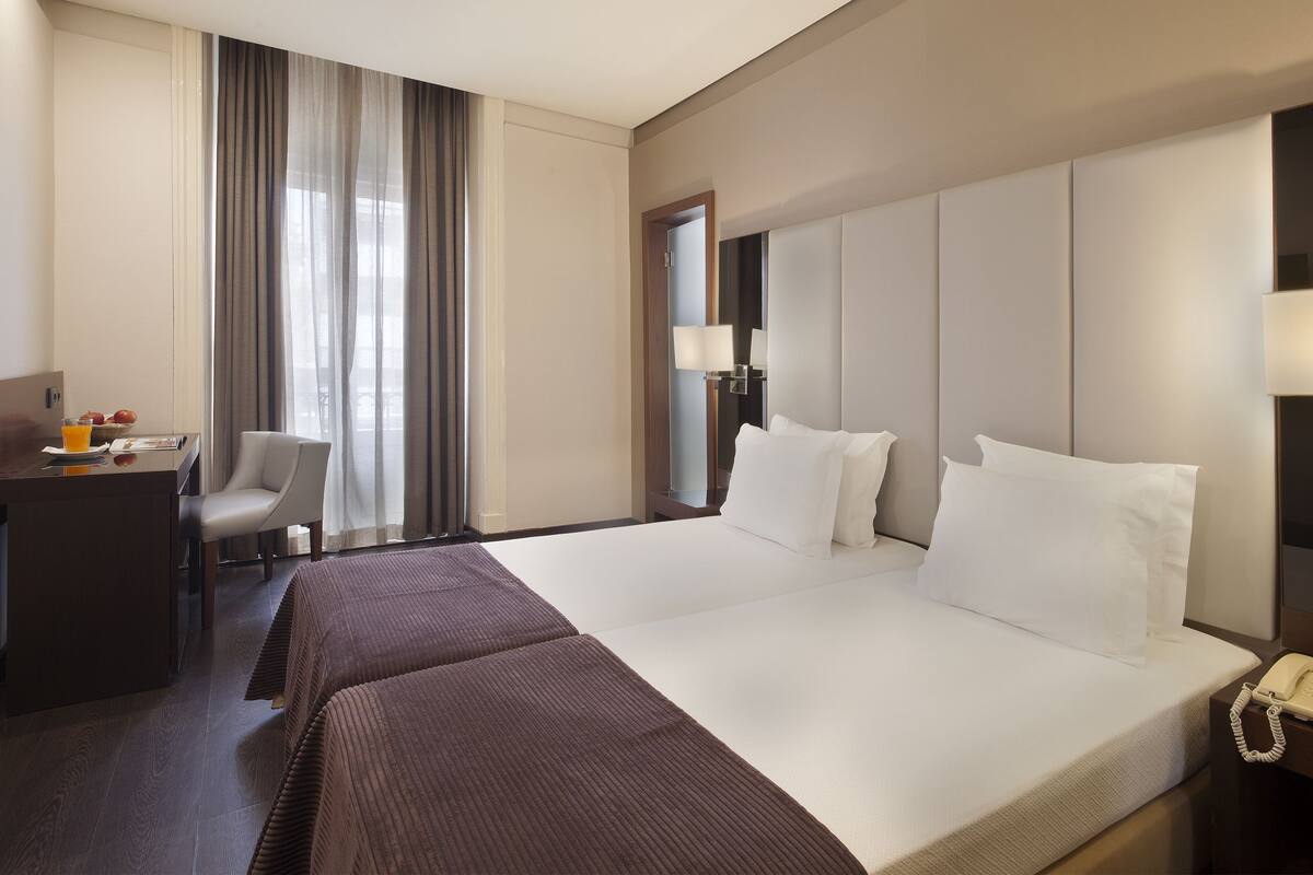 Een hotelkamer met een groot bed, een bureau met telefoon, een stoel en een raam met gordijnen.