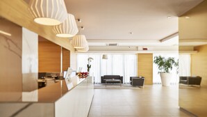 A modern hotel lobby with a reception desk, a sofa, a coffee table, and a potted plant. - Hotel Fonzari (Grado)