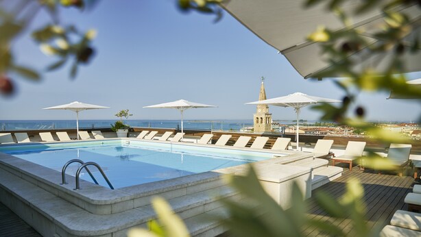 A pool area with lounge chairs and umbrellas, a stone tower in the background, and a clear view of the sea. - Hotel Fonzari (Grado)