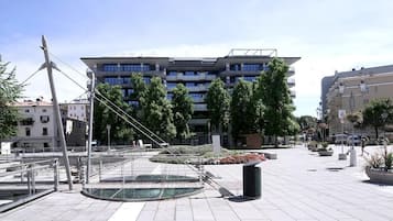 Ein städtischer Platz mit einem modernen Gebäude, einer Skulptur und einem Brunnen.