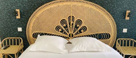 A bed with a woven headboard, two bedside tables, and a wall with a leafy pattern.