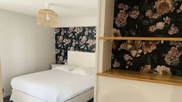 Una cama bien hecha con ropa blanca en una habitación con papel tapiz floral y cabecera de madera.