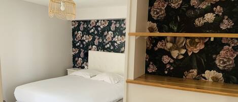 A neatly made bed with white linens in a room with a floral wallpaper and a wooden headboard.