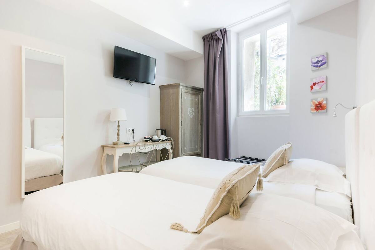 Une chambre d’hôtel avec un lit, un bureau, une télévision et une fenêtre avec des rideaux.