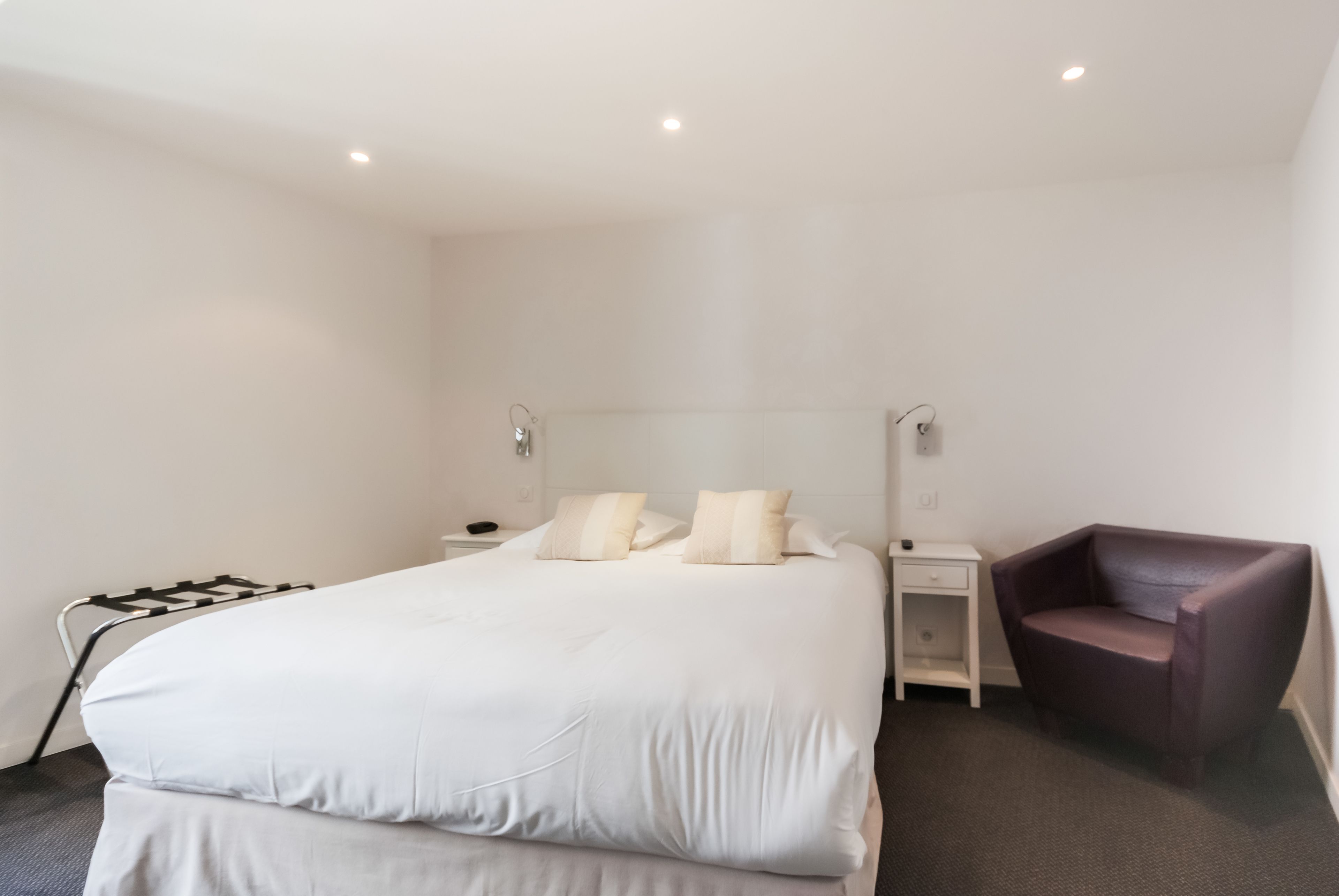 Una habitación de hotel moderna con una cama grande, mesitas de noche, una silla y una lámpara fijada a la pared.